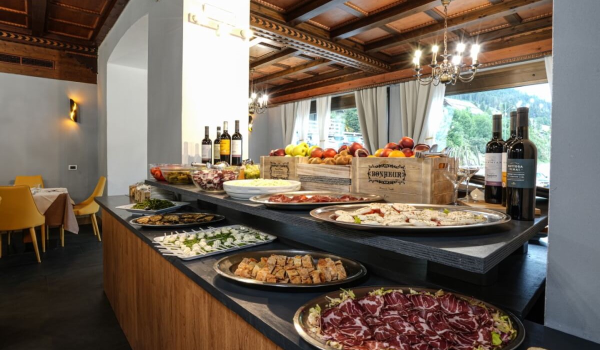 Hotel Monzoni - Bufet bogat cu preparate tradiționale locale, incluzând o gamă variată de aperitive, fructe și vin.