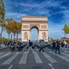 Arcul de Triumf se înalță impunător pe Champs-Élysées, încadrat de copaci și clădiri elegante ce îi subliniază perspectiva și forța simbolică în inima Parisului.