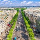 Champs-Élysées se întind ca un bulevard măreț străjuit de copaci, încadrat de clădiri Belle Époque și buticuri elegante, cu monumente istorice ridicându-se în depărtare.