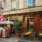 Un restaurant parizian tipic de pe Rue Mouffetard, în Cartierul Latin, își întâmpină oaspeții cu mese în aer liber, arome îmbietoare și atmosfera animată a străduțelor istorice din Paris.