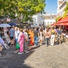 Turiștii la pitoreasca Place du Tertre: printre șevalete colorate, se opresc pentru un portret sau o caricatură, savurează cafeaua pe terasele animate, cufundați în atmosfera vibrantă.