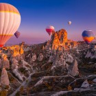Balonurile cu aer cald plutesc peste Cappadocia la apus, oferind priveliști spectaculoase asupra peisajelor lunare, hornurilor de zână și culorilor magice ale cerului.