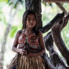 O tânără fată indigenă Wayuri, îmbrăcată în costumul tradițional, sprijinită de un copac în jungla amazoniană ecuadoriană.