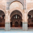 Detalii ale arcadelor din Madrasa Al-Bouanania: decorațiuni elaborate cu motive geometrice, arabescuri florale și caligrafie arabă, artă islamică tradițională.