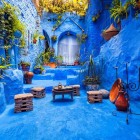 O curte tipică în medina albastră din Chefchaouen, cu oale din teracotă, măsuță și scaune rustice, transmite căldură și autenticitate în tradiția marocană.