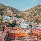 Chefchaouen se deschide între munți cu casele sale albastre strălucitoare care se contopesc în peisaj, oferind o priveliște uluitoare asupra naturii și tradiției marocane.