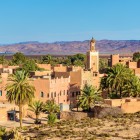 Priveliștea asupra orașului Ouarzazate arată kasbah-uri istorice, clădiri ocru și palmieri, cu Munții Atlas Înalt pe fundal.