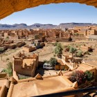 Priveliștea de sus a lui Nkob dezvăluie un labirint de kasbah-uri din pământ roșu printre palmieri și dealuri aride, cu Jbel Saghro dominând orizontul.