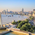 Vedere panoramică a orașului Shanghai cu râul Huangpu care traversează orașul, zgârie-nori moderni și lumini spectaculoase reflectate pe apă.