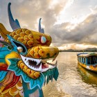 Barcă dragon tradițională pe râul din Hué, simbol al culturii locale, printre ape liniștite, arhitectură istorică și atmosfera imperială vietnameză.