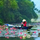 O barcă alunecă liniștită pe lângă o pagodă din Hanoi, printre reflexii aurii și acoperișuri curbe care evocă spiritualitatea vietnameză.