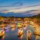 Bărci luminate de felinare navighează pe râul din Hoi An, printre reflexii pe apă și atmosfera romantică a orașului istoric vietnamez.