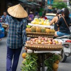 Un vânzător ambulant pe bicicletă transportă fructe tropicale pe străzile din Hanoiul vechi, printre case vechi și viața stradală plină de viață.