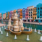 În centrul pieței, fântâna țâșnește printre culorile vii ale zilei, înconjurată de clădiri în stil italian care se reflectă în canal.