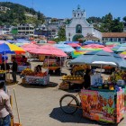 În piața din San Cristóbal de Las Casas, umbrelele colorate îi adăpostesc pe comercianții indigeni care vând produse artizanale și alimente locale, formând un mozaic viu de cultură, tradiție și culoare.