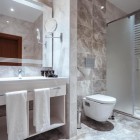 Baie modernă și elegantă cu duș din sticlă, finisaje tip marmură, chiuvetă spațioasă și oglindă iluminată. Spațiu luminos, rafinat și confortabil.