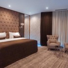 Cameră matrimonială elegantă și modernă, cu pat king size, tăblie tapițată, mobilier rafinat și zonă de relaxare cu fotolii. Spațiu luminos, confortabil și atent amenajat.