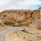 Mausoleul Diri Baba din Azerbaidjan, săpat în stâncă, domină un peisaj arid cu scară istorică, drum panoramic și coline cu farmec sugestiv.