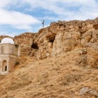 Mausoleul Diri Baba, săpat în stâncă în Azerbaidjan, prezintă o cupolă albă, arcade din piatră și un peisaj arid cu coline și stânci sugestive.