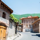 Case istorice tipice din Sheki, Azerbaidjan, cu fațade din piatră și cărămidă, balcoane din lemn și acoperișuri tradiționale, încadrate de colinele verzi ale Caucazului Înalt.