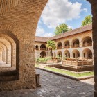 Porticuri și arcade din piatră se deschid spre curtea Caravanseraiului din Sheki, cu grădină centrală și atmosferă istorică în inima Caucazului.