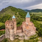 Vedere aeriană a fortăreței Gremi din Kakheti: turnuri din piatră și biserică cu acoperișuri din teracotă domină colina, între văi verzi și munții Georgiei de Est.