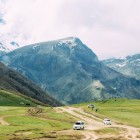 Urcare cu minivan 4x4 prin pajiști alpine și drumuri de munte spre Biserica Sfânta Treime din Gergeti, cu panorame spectaculoase asupra Muntelui Kazbek și vârfurilor Caucazului Mare.