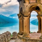 Vedere panoramică de la Fortăreața Ananuri asupra lacului Zhinvali: arcadele vechi din piatră încadrează apele turcoaz și munții Caucazului, creând un peisaj spectaculos.