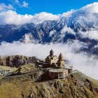 Biserica Sfânta Treime din Gergeti se ridică printre nori la poalele Muntelui Kazbek, dominând peisajele Marelui Caucaz, înconjurată de vârfuri mărețe și liniște alpină.
