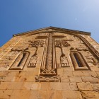 Detaliu al crucii sculptate pe fațada bisericii din Ananuri: basoreliefuri medievale rafinate decorează piatra, mărturie a artei sacre georgiene din secolul al XVII-lea.