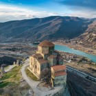 Vedere aeriană a Mănăstirii Jvari deasupra orașului Mtskheta, în locul unde se întâlnesc râurile Kura și Aragvi, înconjurată de munții Caucaz și peisaje spectaculoase din Georgia.