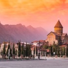 Catedrala Svetitskhoveli din Mtskheta la apus, învăluită în lumini aurii, cu Munții Caucaz în fundal și atmosfera fermecătoare a vechii capitale a Georgiei.