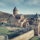Vedere aeriană a Catedralei Svetitskhoveli din Mtskheta, capodoperă a arhitecturii medievale georgiene, înconjurată de ziduri vechi și dealurile văii râului Mtkvari.