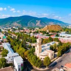 Vedere aeriană a orașului Gori, Georgia, cu istorica Cetate Gori dominând orașul de pe deal, înconjurată de cartiere moderne și munții Caucaz.