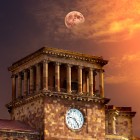 Turnul cu ceas al clădirii Guvernului din Piața Republicii din Erevan, Armenia, luminat de culorile apusului, cu luna care apare pe cer în fundal.