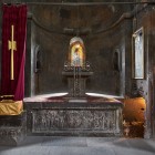 Interiorul Mănăstirii Khor Virap cu altar din piatră, icoane sacre și lumină difuză ce creează o atmosferă liniștită și spirituală, tipică arhitecturii armene.