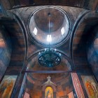 Interiorul Mănăstirii Khor Virap cu bolți din piatră și cupolă centrală pe tambur, linii simple și lumină difuză ce creează o atmosferă spirituală.