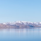 Priveliște asupra Lacului Sevan, Armenia: ape liniștite și cristaline reflectă munții înzăpeziți, creând un peisaj alpin spectaculos și una dintre cele mai iconice destinații naturale.
