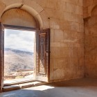 Priveliște din bisericile Mănăstirii Noravank, Armenia: ușă sculptată deschisă spre munții canionului Vayots Dzor, lumină naturală și peisaje spectaculoase.