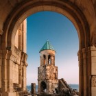 Arcul din piatră fin sculptat încadrează clopotnița Catedralei Bagrati. Liniile armonioase și detaliile medievale evidențiază eleganța arhitecturii georgiene.