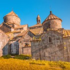 Vedere asupra Mănăstirii Haghpat din Armenia, cu biserici din piatră și cupole conice luminate de lumina aurie, evidențiind detalii medievale și o atmosferă sugestivă.