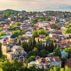 Peisaj matinal splendid al centrului istoric din Kutaisi, Georgia, cu catedrala catolică în prim-plan, înconjurată de copaci verzi și munți în fundal.