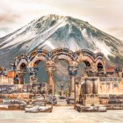 Ruinele antice ale Catedralei Zvartnots din Armenia, cu arcade elegante din piatră sculptată, pe fundalul impunătorului Munte Ararat acoperit de zăpadă.