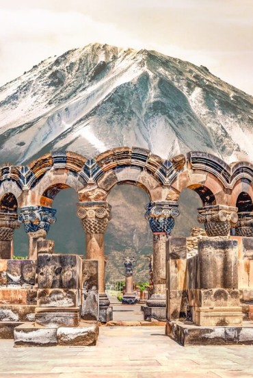 Ruinele antice ale Catedralei Zvartnots din Armenia, cu arcade elegante din piatră sculptată, pe fundalul impunătorului Munte Ararat acoperit de zăpadă.