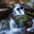 Cascada Gveleti din Defileul Dariali: apa limpede curge peste roci acoperite de mușchi și frunze de toamnă, creând o atmosferă proaspătă și spectaculoasă în inima naturii georgiene.