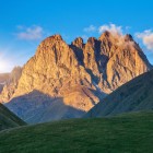 Vârfurile impunătoare ale Muntelui Chaukhebi strălucesc în lumina aurie a apusului, dominând văi alpine și peisaje spectaculoase în Parcul Național Kazbegi.