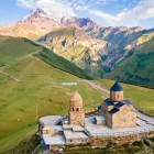Biserica Sfânta Treime din Gergeti domină dealurile de deasupra Stepantsminda, privind peste văile din Kazbegi, cu Muntele Kazbek în fundal.