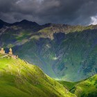 Biserica Sfânta Treime din Gergeti domină dealurile din Kazbegi, între pajiști verzi și crestele impunătoare ale Caucazului de la orizont.