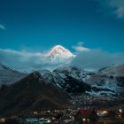La Stepantsminda, Muntele Kazbek și pitoreasca Biserică Gergeti se luminează în lumina dimineții, oferind un peisaj fermecător printre munții Caucazului.