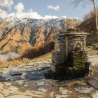 Fântână veche din piatră lângă Biserica din Gergeti, cu apă de izvor ce curge printre munții Caucaz și priveliști largi asupra văii Kazbegi.